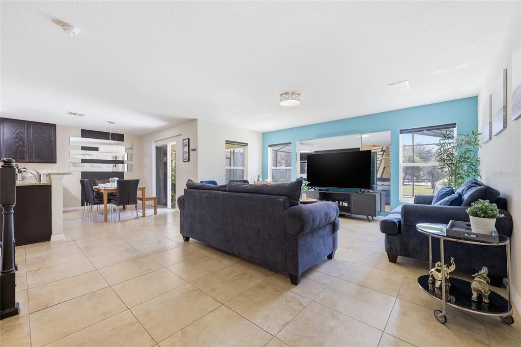 A living room with tile floors, a blue accent wall, and a dining area nearby — 2620 SANTOSH COVE, KISSIMMEE, FL