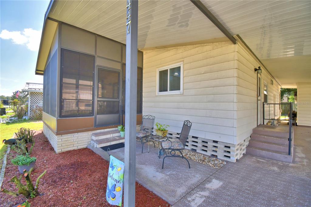 A mobile home exterior features a screened porch, a concrete patio, and a covered carport — 447 VILLAGE CIRCLE SW, WINTER HAVEN, FL