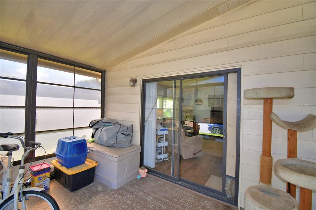 A covered patio features a sliding glass door, a cat tree, and a storage bin — 447 VILLAGE CIRCLE SW, WINTER HAVEN, FL