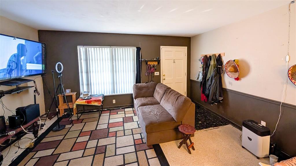 A living room features a brown sofa, a patterned area rug, and a wall-mounted television — 1590 PEACEFUL LANE N, CLEARWATER, FL