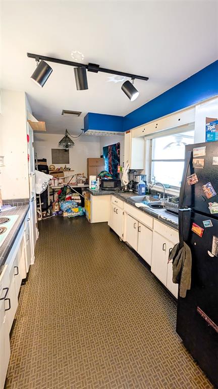 A kitchen features white cabinets, a black refrigerator, patterned flooring, and a track lighting fixture — 1590 PEACEFUL LANE N, CLEARWATER, FL