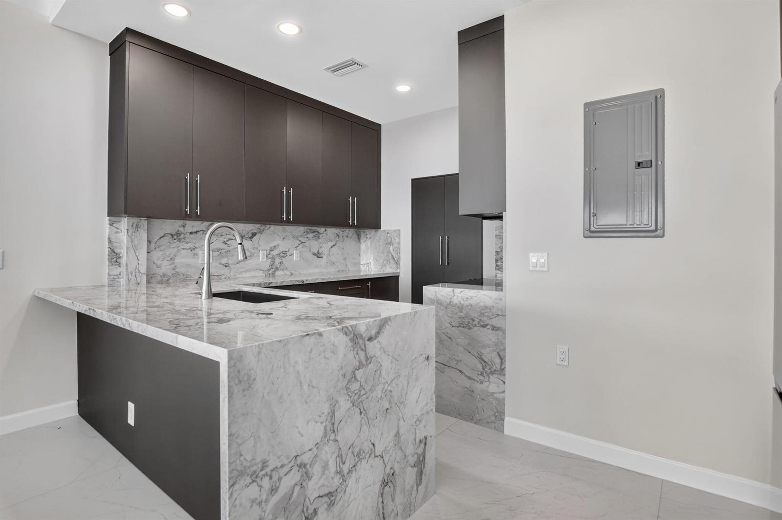 A modern kitchen features dark cabinetry, marble countertops, and a waterfall island — 19317 Sabal Lake Drive # 5066, Boca Raton FL 33434, BOCA RATON, FL