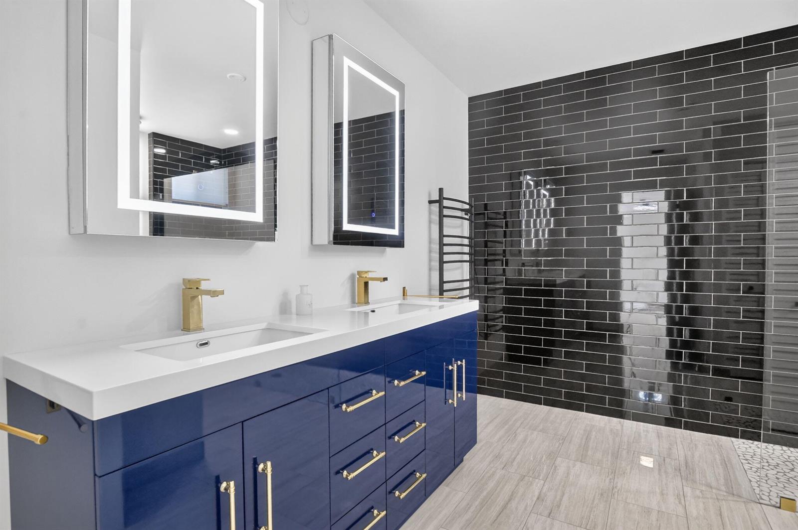 A modern bathroom features a blue double vanity, gold hardware, LED mirrors, and black tile — 19317 Sabal Lake Drive # 5066, Boca Raton FL 33434, BOCA RATON, FL