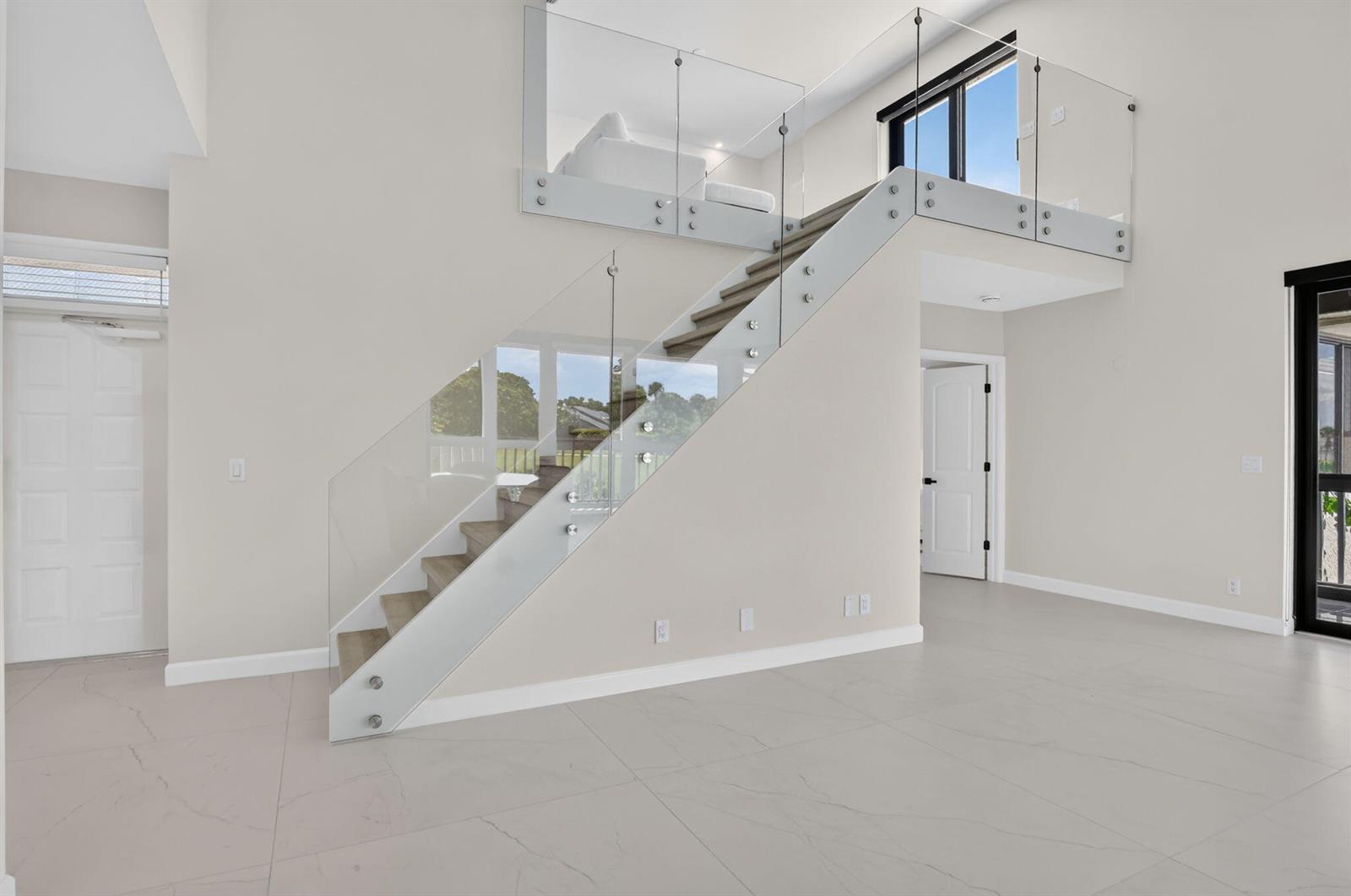 A modern living room features a floating staircase with glass railings and light tile flooring — 19317 Sabal Lake Drive # 5066, Boca Raton FL 33434, BOCA RATON, FL