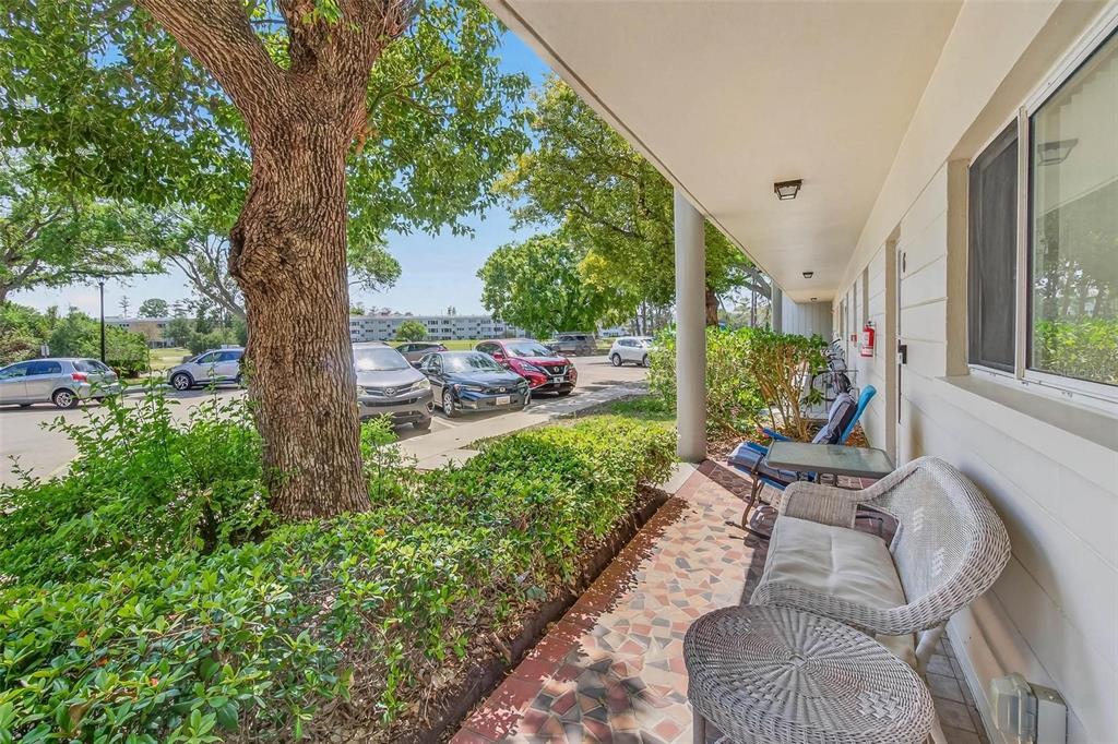 A covered patio with wicker furniture overlooks a parking lot and green trees — 2440 WORLD PARKWAY BOULEVARD UNIT 6, CLEARWATER, FL
