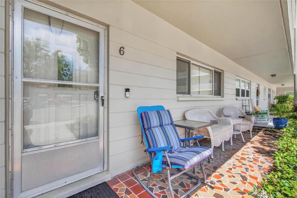 A covered patio features a tiled floor, a blue striped chair, and white wicker furniture — 2440 WORLD PARKWAY BOULEVARD UNIT 6, CLEARWATER, FL