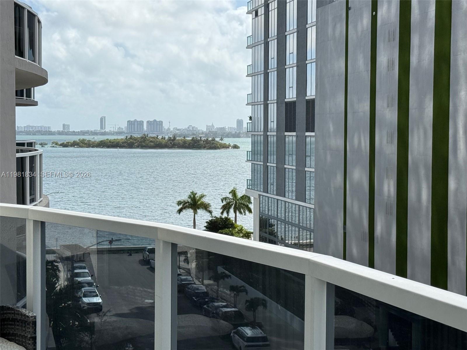 A balcony view overlooks a bay, palm trees, a neighboring high-rise, and a city skyline — 601 NE 23rd St # 605, Miami FL 33137, MIAMI, FL
