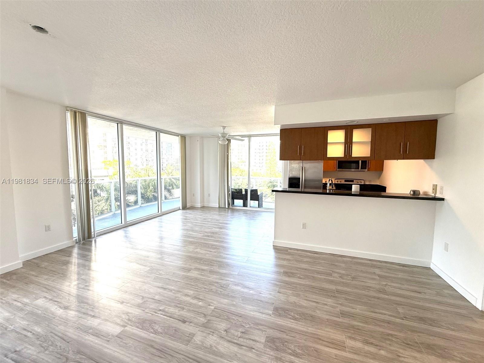 An open-concept living area features light wood-look flooring, a kitchen with dark cabinets, and balconies — 601 NE 23rd St # 605, Miami FL 33137, MIAMI, FL