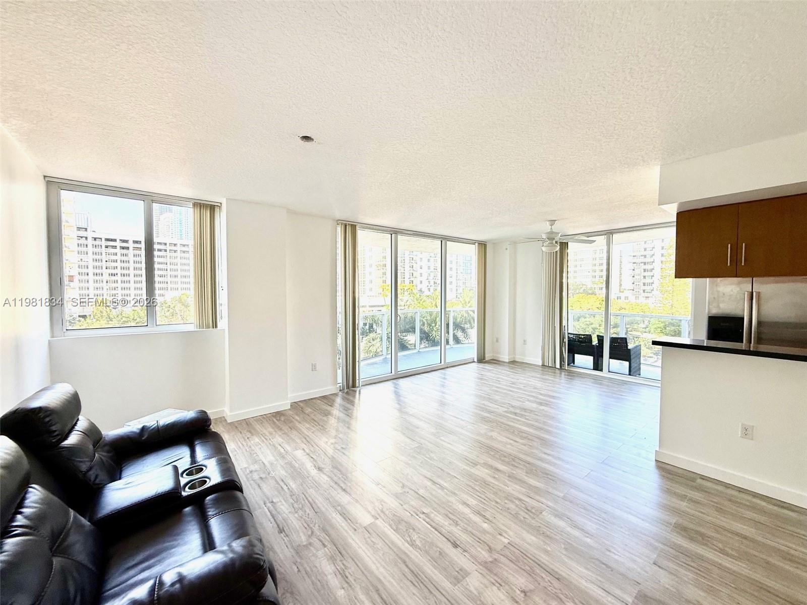 A living room features light wood-look flooring, large windows, and a partial kitchen view — 601 NE 23rd St # 605, Miami FL 33137, MIAMI, FL