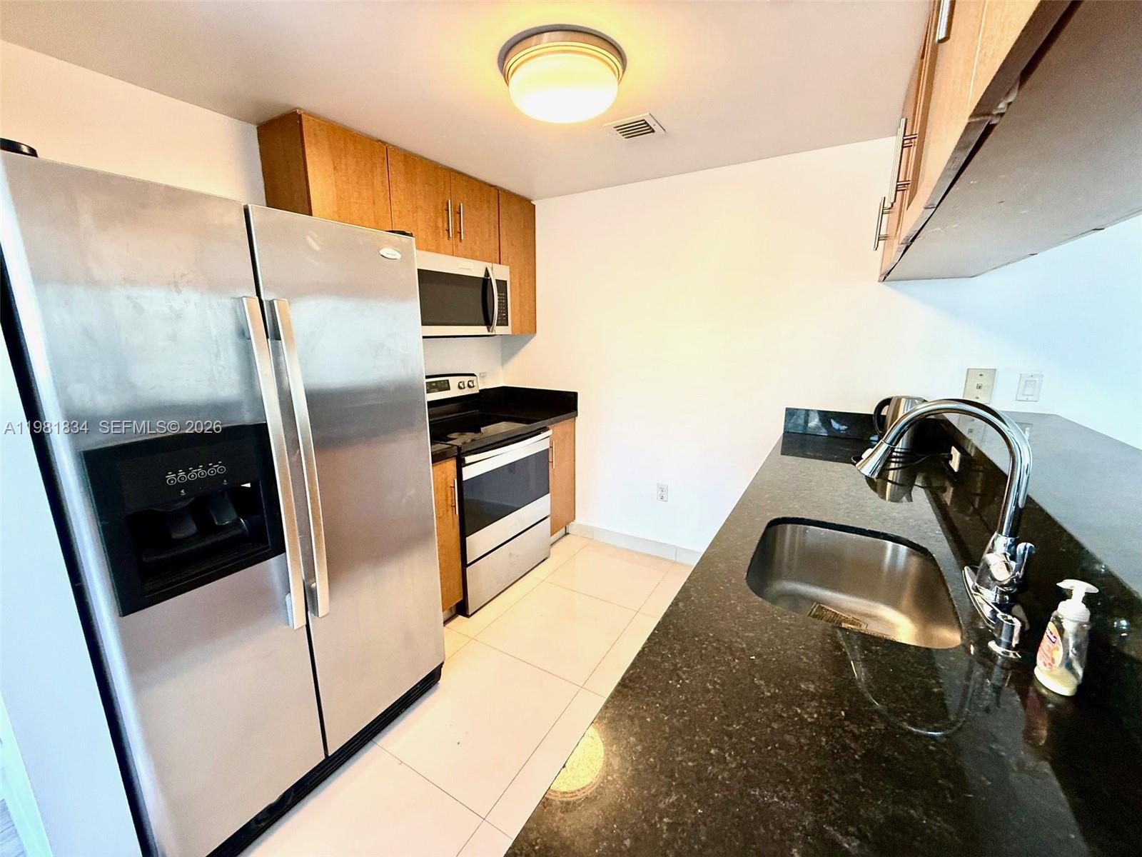 A kitchen features stainless steel appliances, wood cabinets, and dark granite countertops — 601 NE 23rd St # 605, Miami FL 33137, MIAMI, FL