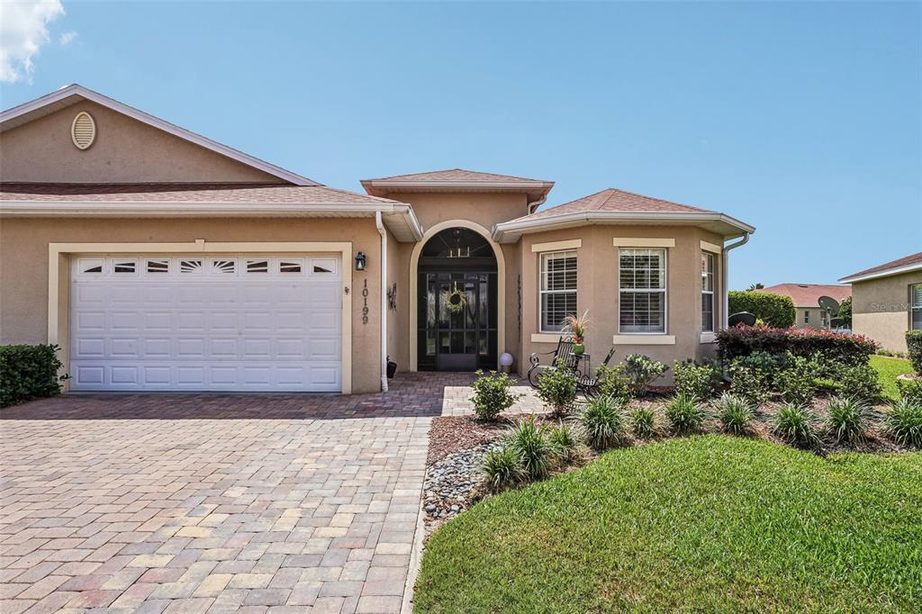 The exterior of a tan stucco house features a paver driveway, garage, and arched entryway — 10199 MAINSAIL DRIVE, OXFORD, FL