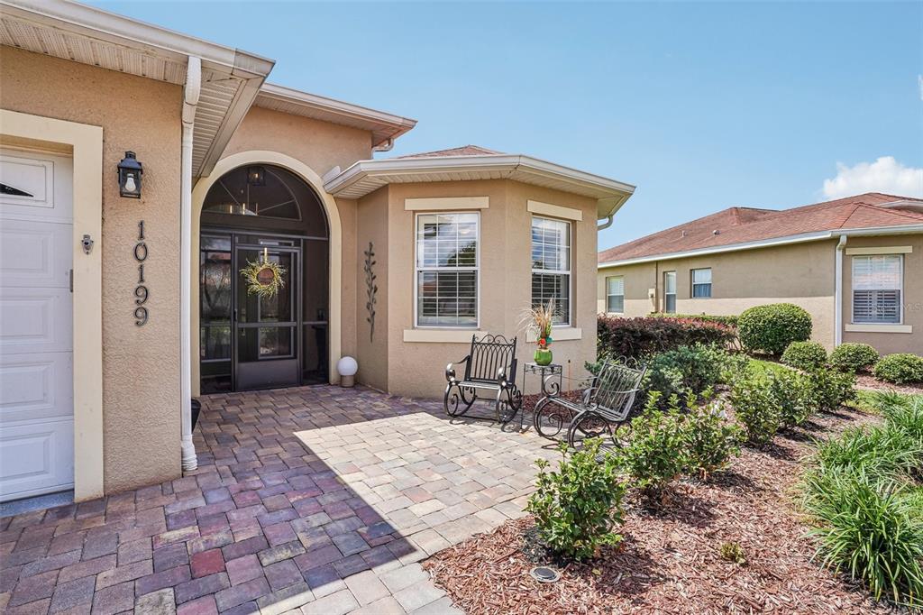 The exterior of a tan stucco house features a paver patio and a screened entryway — 10199 MAINSAIL DRIVE, OXFORD, FL