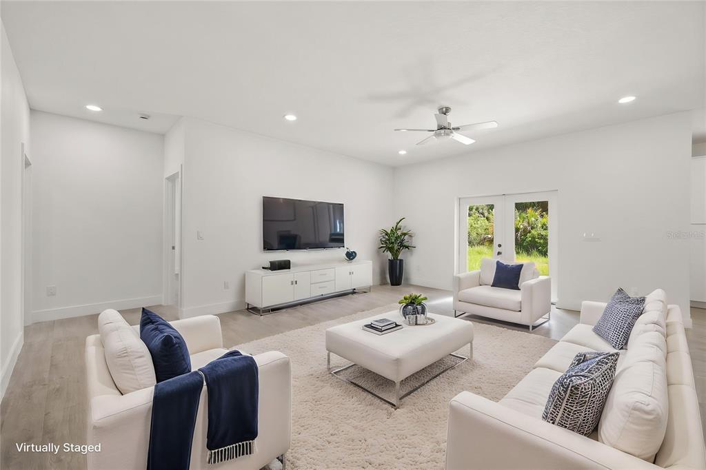 A living room with white furniture, a large television, and glass doors leading outside — 2769 HAGUE STREET SW, PALM BAY, FL