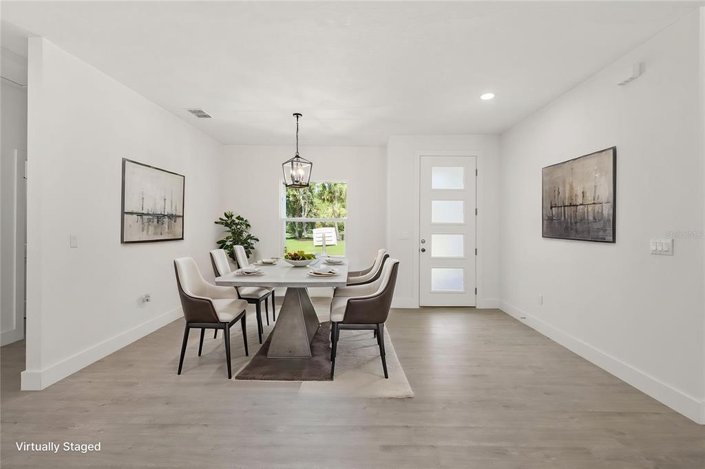 A dining room with light wood-look flooring, a modern table, and a white front door — 2769 HAGUE STREET SW, PALM BAY, FL