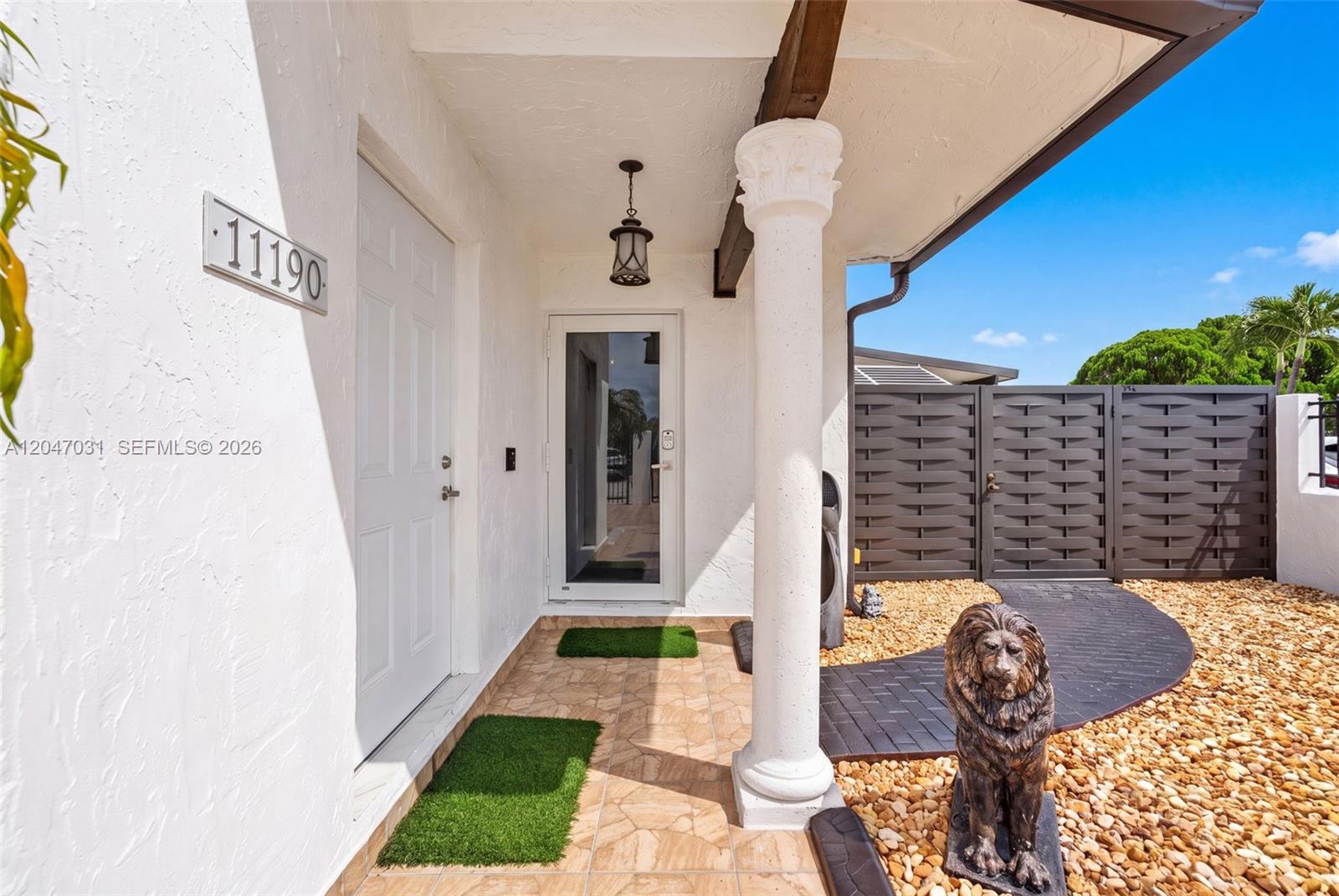 A white house entrance features a tiled porch, a decorative column, and a lion statue — 1635 SW 138th Ct, Miami FL 33175, MIAMI, FL