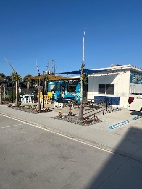 An outdoor patio area with tables, chairs, and palm trees sits beside a white building — 323 FLAGLER AVENUE, NEW SMYRNA BEACH, FL