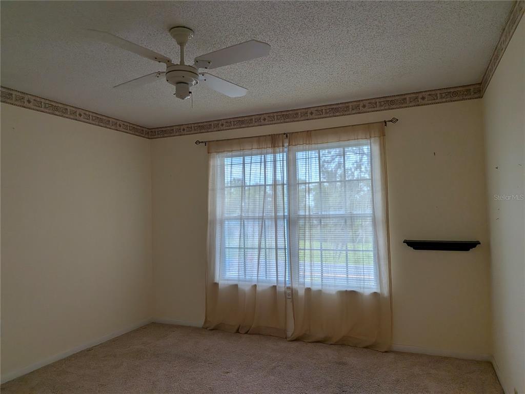 An empty bedroom features beige carpet, cream walls, a ceiling fan, and a window with curtains — 2400 FOREST DRIVE UNIT 261, INVERNESS, FL
