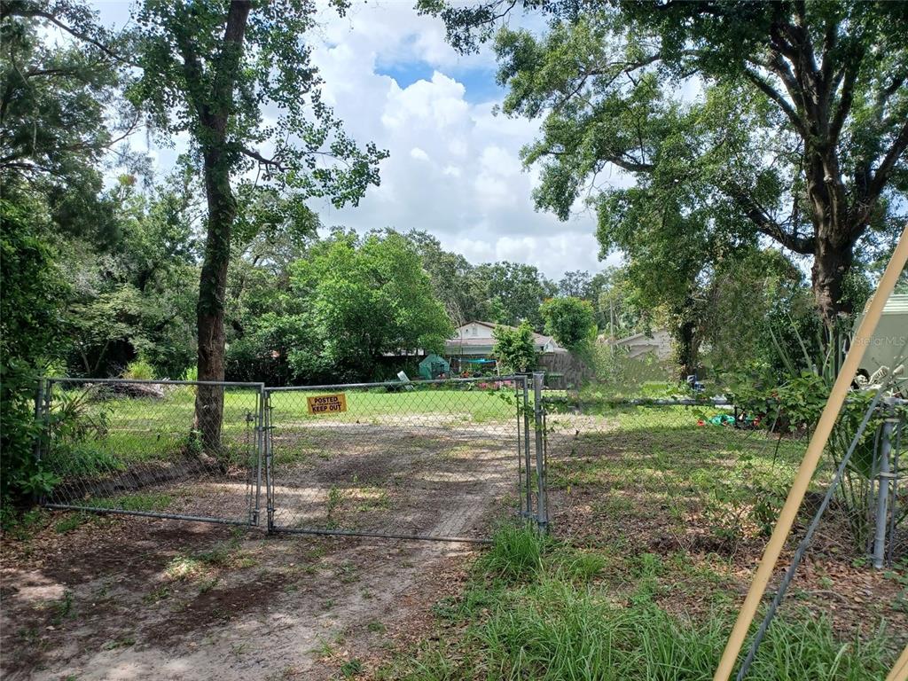 A chain-link fence with a gate encloses a dirt driveway leading to a grassy lot — 1802 E FAIRBANKS STREET, TAMPA, FL