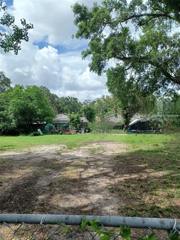 A grassy, partially shaded vacant lot viewed from behind a chain-link fence — 1802 E FAIRBANKS STREET, TAMPA, FL