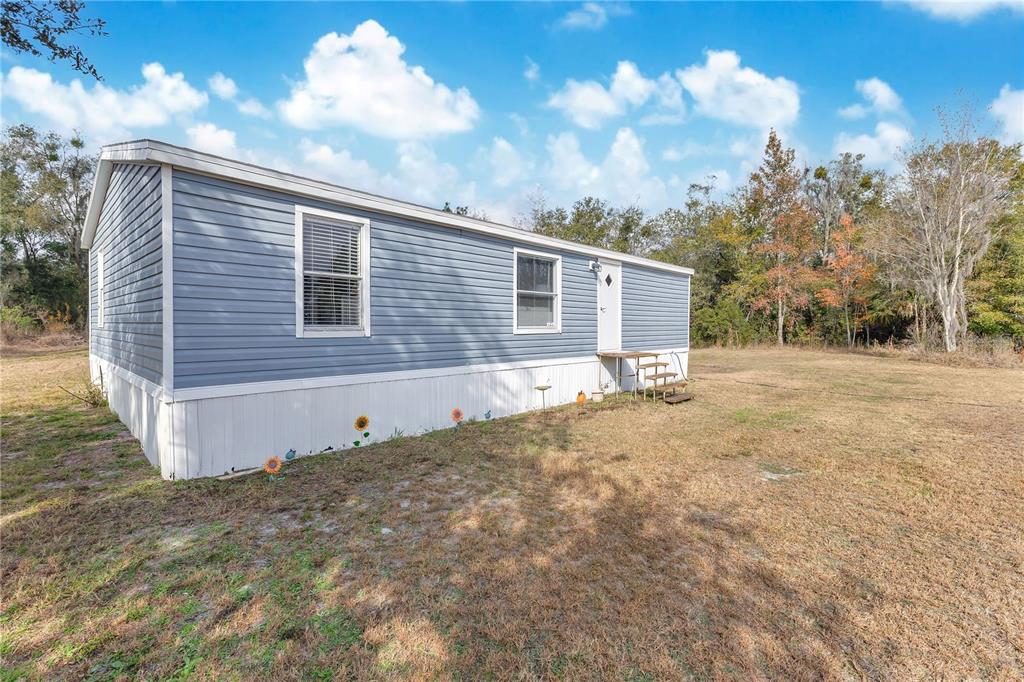 A blue-sided mobile home sits on a grassy lot with a small wooden entry step — 10810 SPORTSMAN TRAIL, LAKELAND, FL