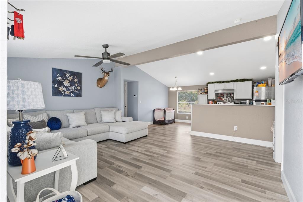 A living room with light gray walls, wood-look flooring, and an open kitchen beyond — 10810 SPORTSMAN TRAIL, LAKELAND, FL