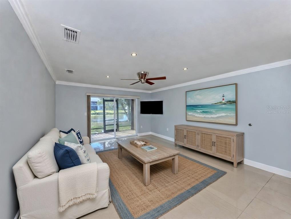 A living room with a beige sofa, wooden coffee table, media console, and sliding glass doors — 2616 HIDDEN LAKE DRIVE N UNIT A, SARASOTA, FL