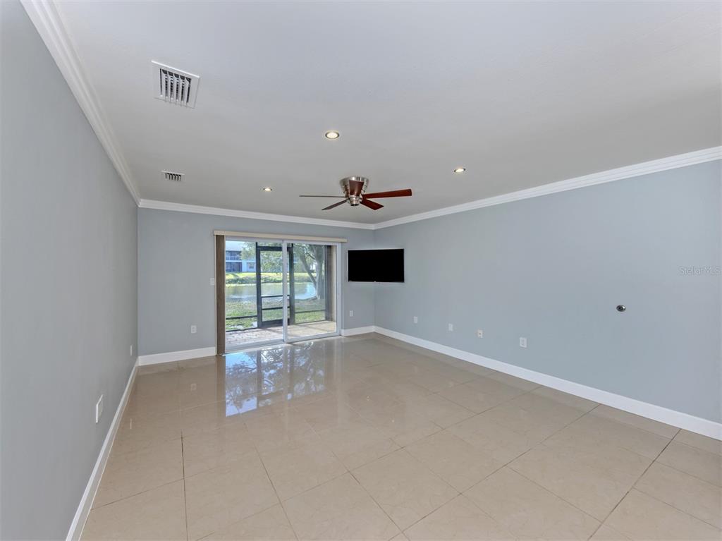 A spacious living room with light blue walls, tile flooring, a ceiling fan, and sliding doors — 2616 HIDDEN LAKE DRIVE N UNIT A, SARASOTA, FL