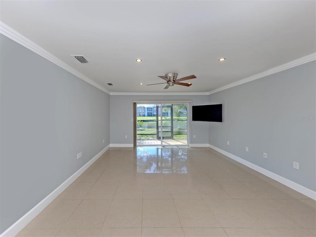 A spacious living room with light gray walls, tile flooring, a ceiling fan, and sliding doors — 2616 HIDDEN LAKE DRIVE N UNIT A, SARASOTA, FL