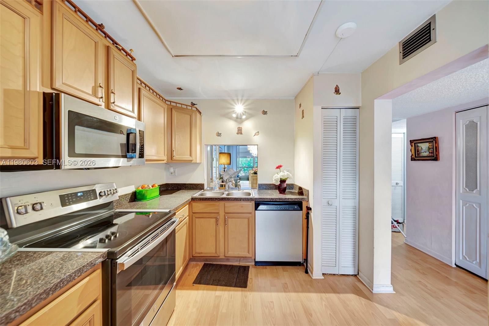 A kitchen features light wood cabinets, stainless steel appliances, and a pass-through window — 3940 Inverrary Blvd # A, Lauderhill FL 33319, LAUDERHILL, FL