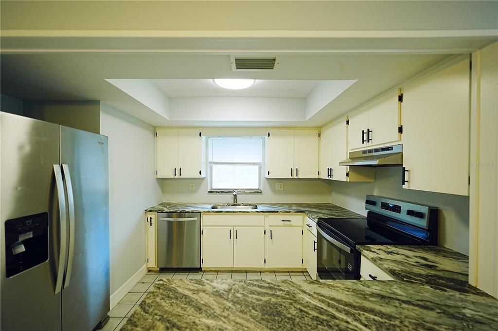 A kitchen features white cabinets, granite countertops, stainless steel appliances, and a tiled floor — 1882 RITA STREET, SARASOTA, FL