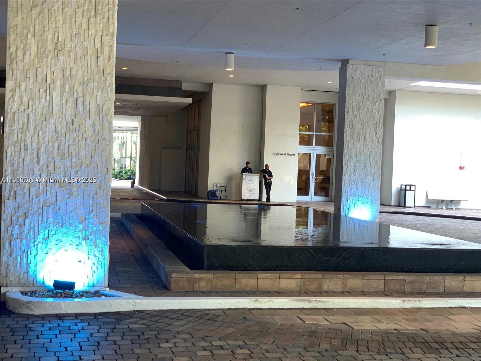 A modern building entrance features a stone-clad pillar, a reflecting pool, and two security personnel — 1060 Brickell Ave # 1701, Miami FL 33131, MIAMI, FL