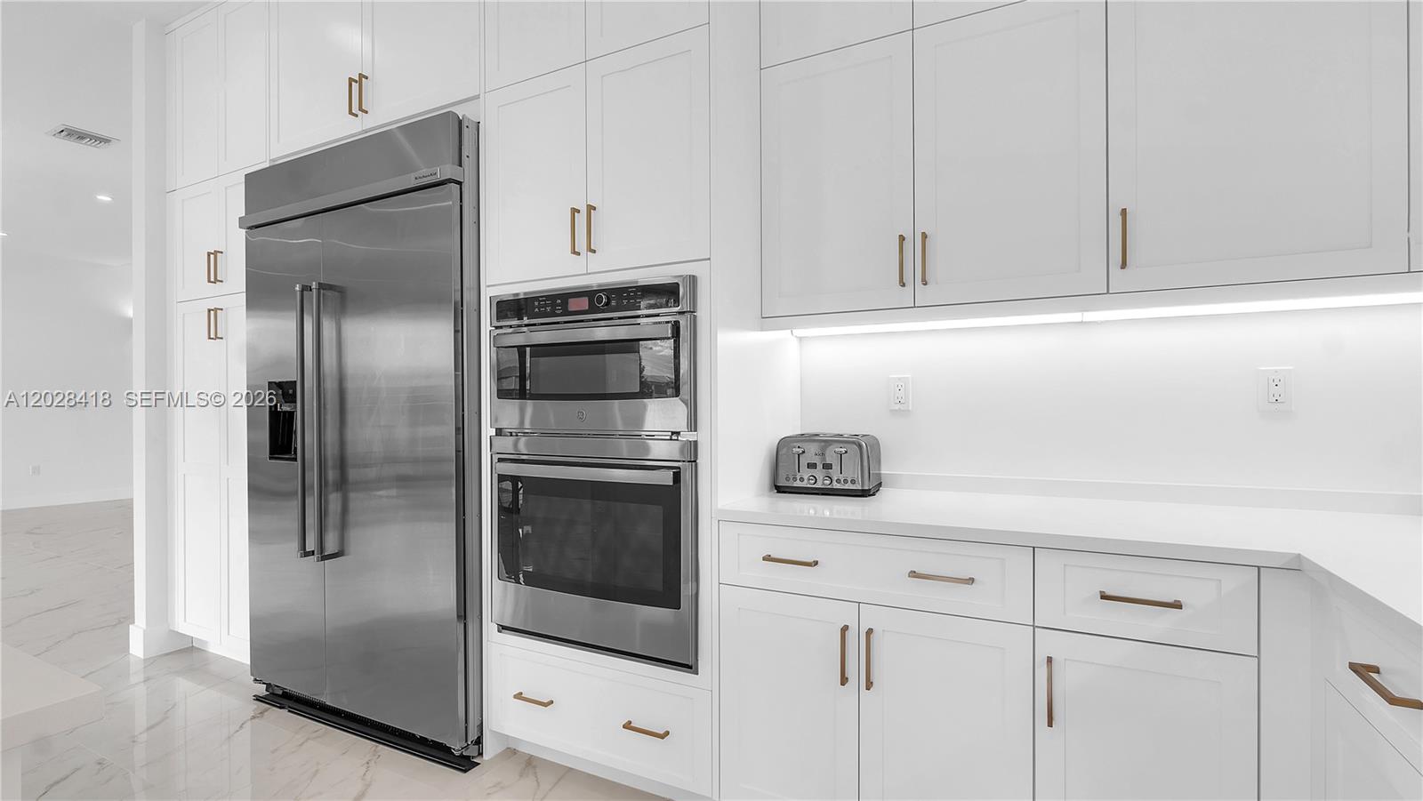 A modern kitchen features white cabinetry, stainless steel appliances, and a marble-patterned floor — 20284 Bandon Dunes Rd, Boca Raton FL 33434, BOCA RATON, FL