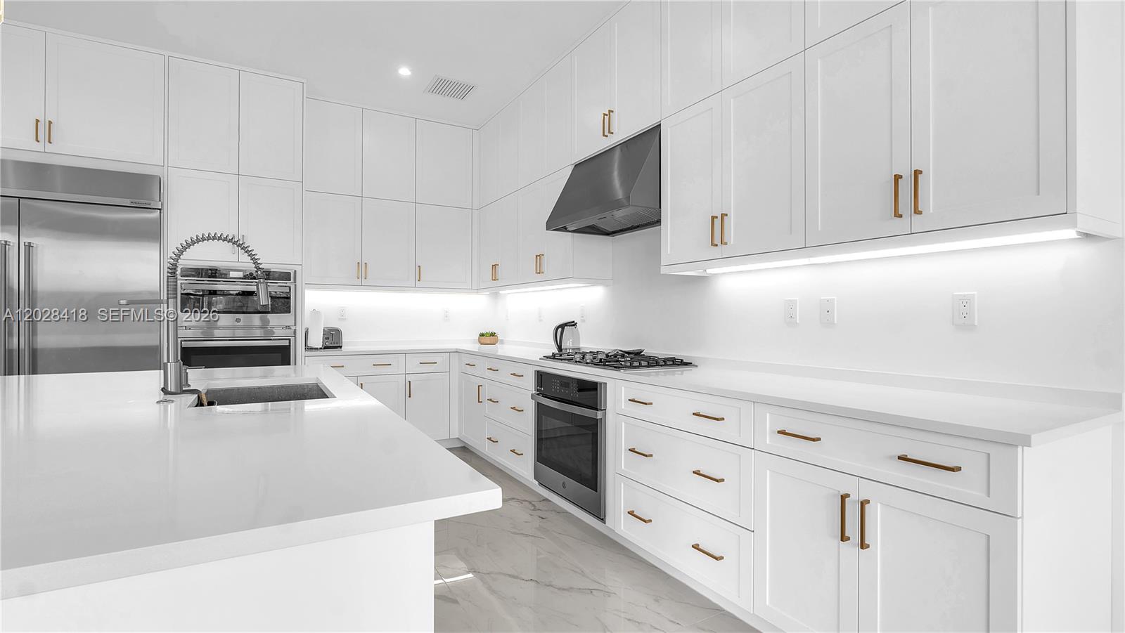 A modern white kitchen features marble countertops, stainless steel appliances, and gold cabinet hardware — 20284 Bandon Dunes Rd, Boca Raton FL 33434, BOCA RATON, FL
