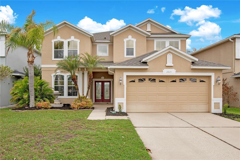 A two-story tan stucco house with a two-car garage and a front yard with palms — 2615 LAKEMOOR DRIVE, ORLANDO, FL