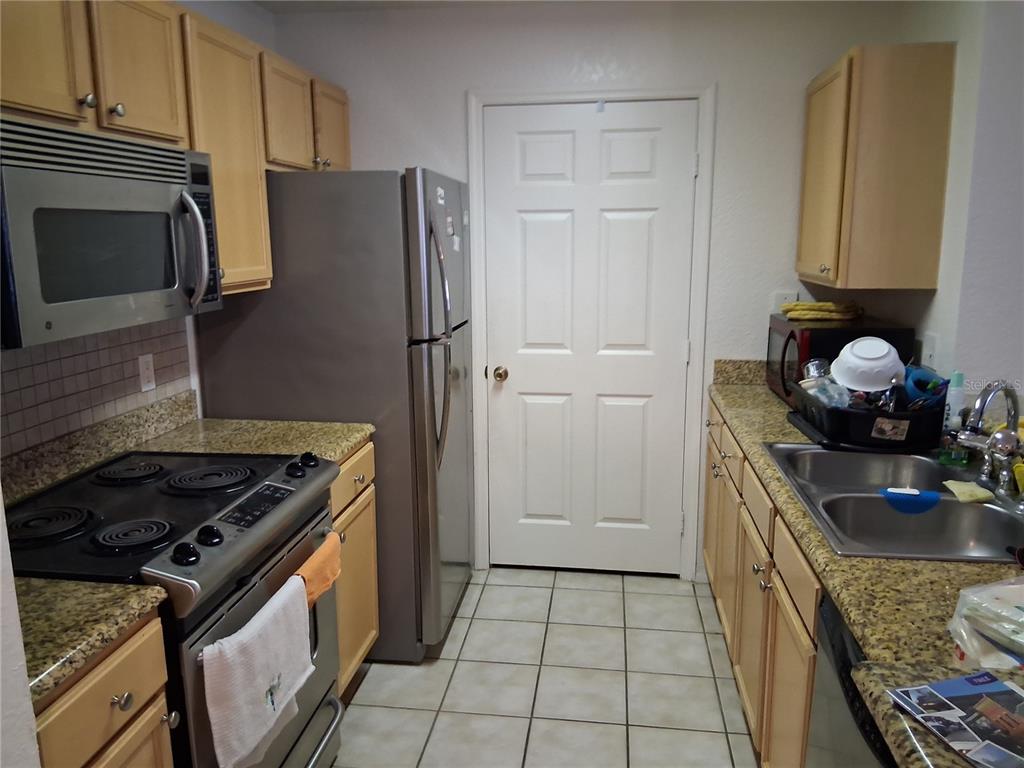 A galley kitchen features light wood cabinets, granite countertops, stainless steel appliances, and tile flooring — 2763 LIGHTHOUSE COVE ROAD UNIT 6-204, ORANGE CITY, FL