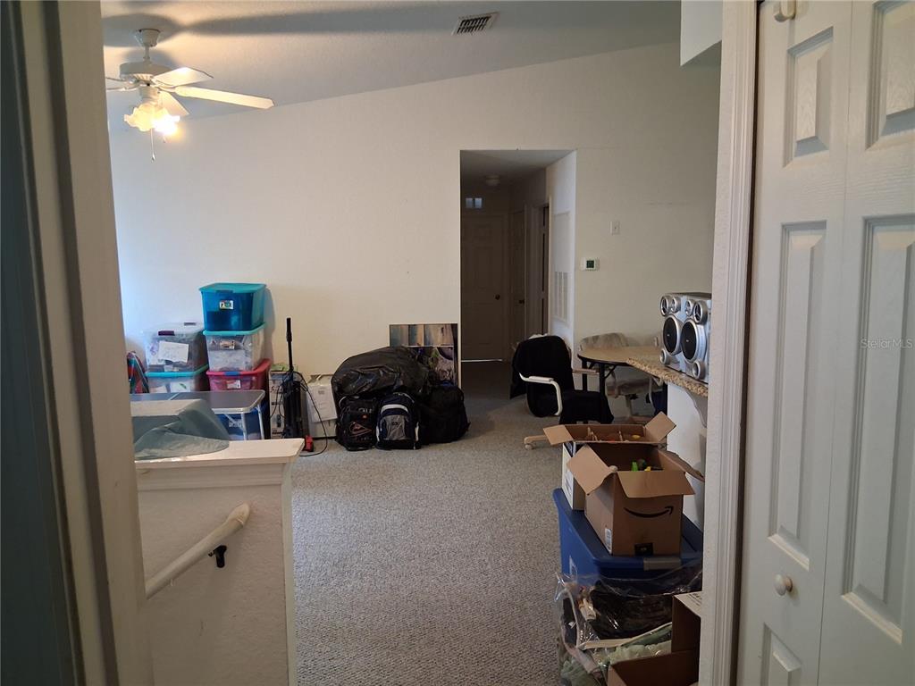 A carpeted room with a ceiling fan, storage bins, and a doorway leading to a hallway — 2763 LIGHTHOUSE COVE ROAD UNIT 6-204, ORANGE CITY, FL