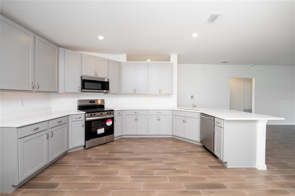 A kitchen features light gray cabinets, stainless steel appliances, white countertops, and wood-look tile flooring — 213 HARPER ESTATES CIRCLE, LAKE WALES, FL