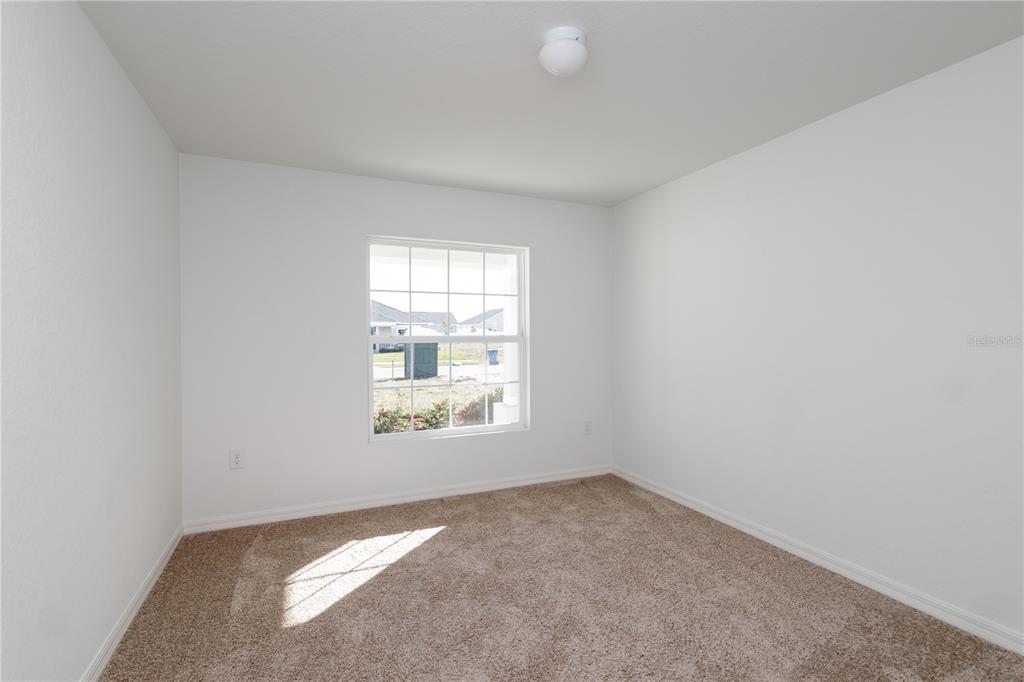 An empty bedroom features white walls, tan carpet, a single window, and a ceiling light — 213 HARPER ESTATES CIRCLE, LAKE WALES, FL