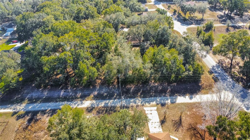 An aerial view shows a wooded lot with a dirt road and a concrete driveway — SW 109TH PLACE, DUNNELLON, FL