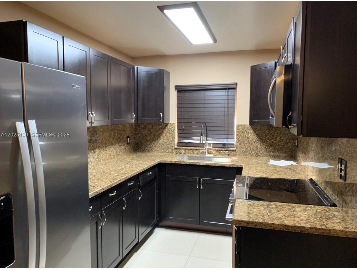 A kitchen features dark wood cabinets, granite countertops, and a stainless steel Samsung range — FORT LAUDERDALE, FL