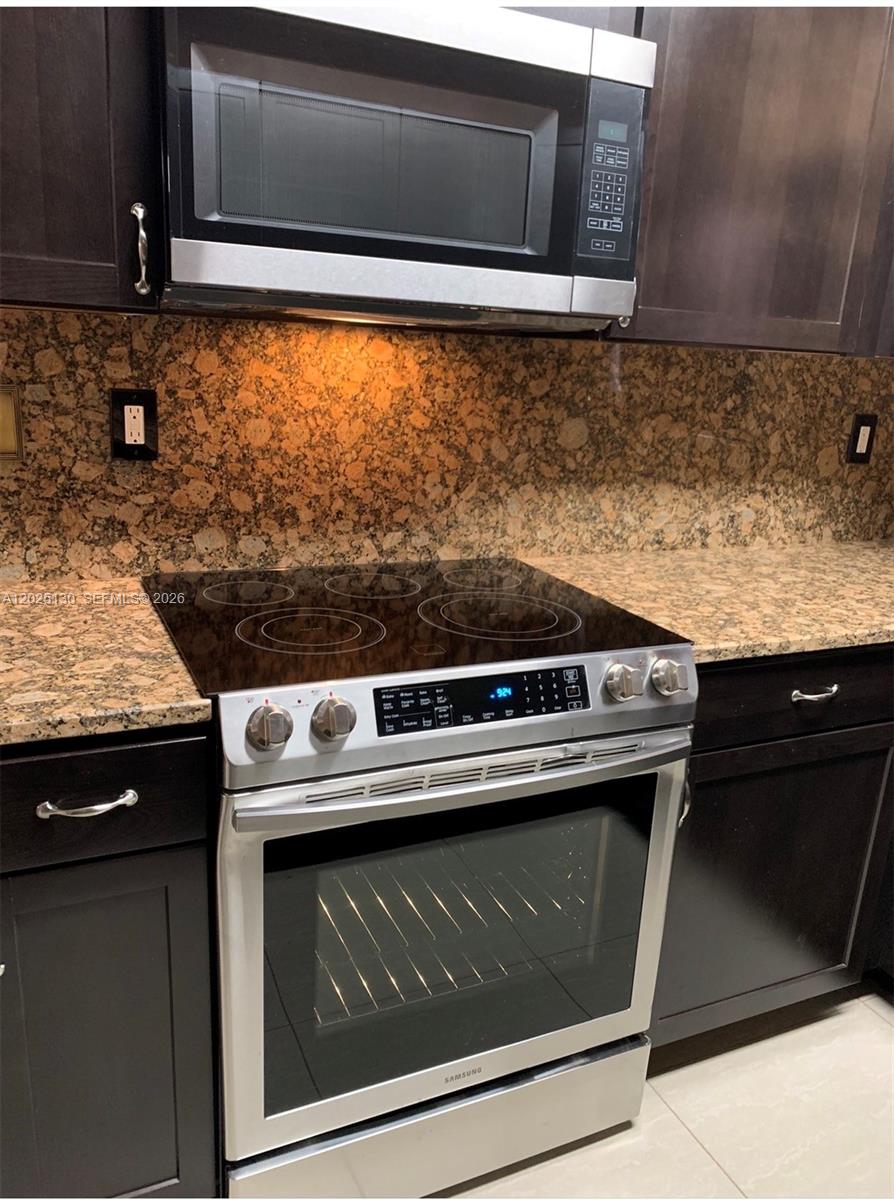 A laundry room features dark appliances, a wire shelf, and a brown door on tile floors — FORT LAUDERDALE, FL