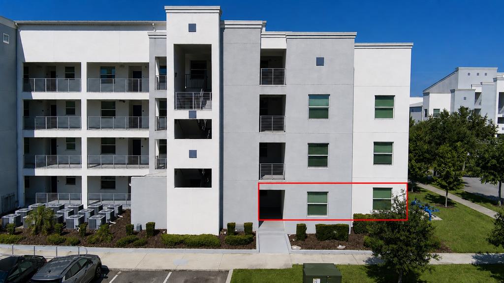 Exterior view of a multi-story apartment building with a red rectangle highlighting a ground-floor unit — 3111 PARADOX CIRCLE UNIT 108, KISSIMMEE, FL