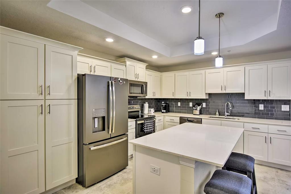 A modern kitchen features white cabinetry, stainless steel appliances, a center island, and dark tile backsplash — 3111 PARADOX CIRCLE UNIT 108, KISSIMMEE, FL