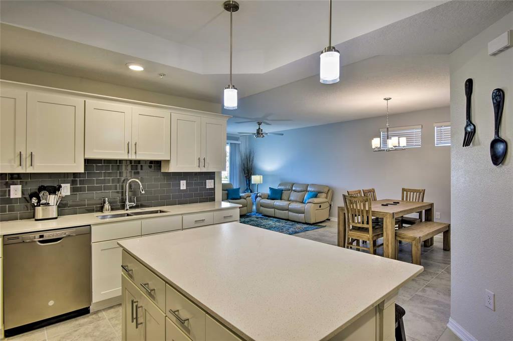 A kitchen with white cabinets and a quartz island overlooks a dining area and living room — 3111 PARADOX CIRCLE UNIT 108, KISSIMMEE, FL