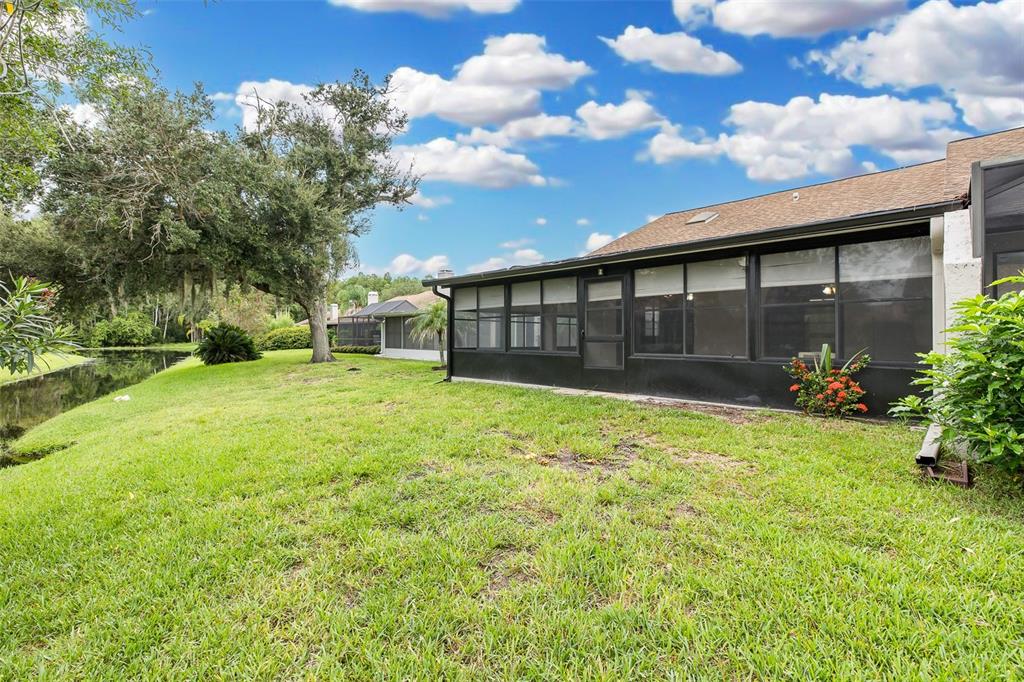 The exterior of a house features a screened-in porch overlooking a grassy lawn and pond — 5508 SALEM SQUARE DRIVE S, PALM HARBOR, FL