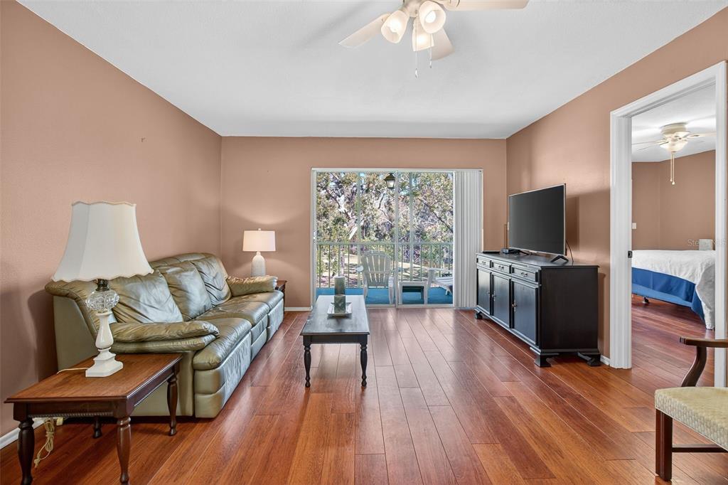 A living room with hardwood floors, a leather sofa, and a sliding door to a balcony — 208 CYPRESS COURT, OLDSMAR, FL