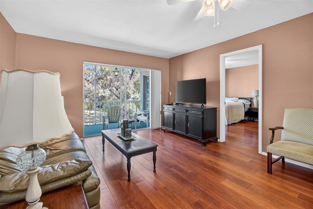 A living room features hardwood floors, a television on a black console, and a screened balcony — 208 CYPRESS COURT, OLDSMAR, FL