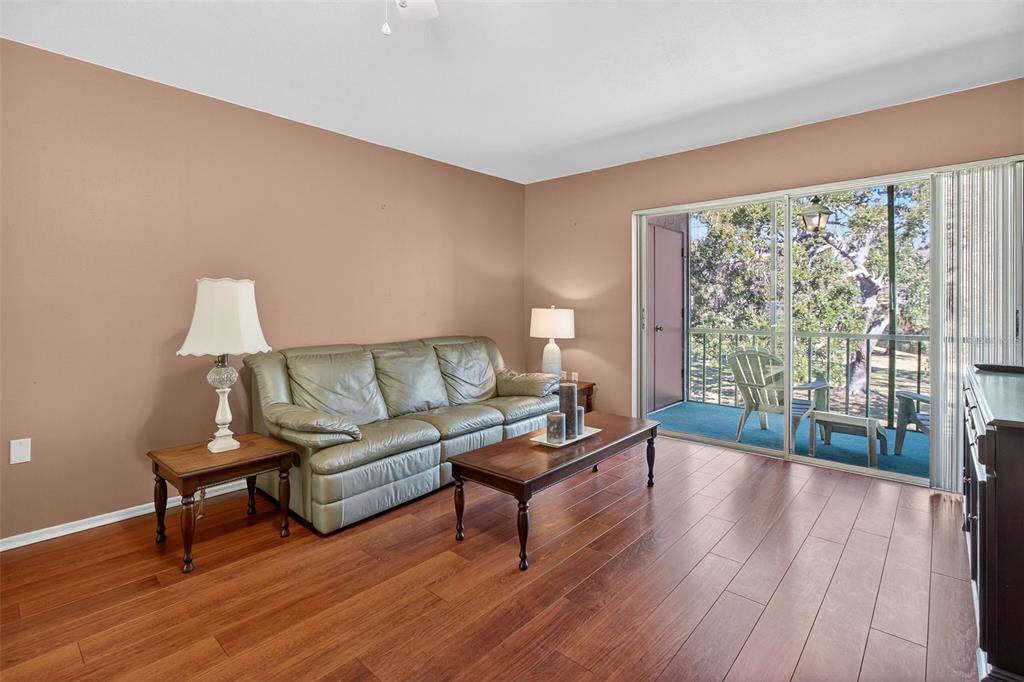A living room with wood flooring, a leather sofa, and a sliding glass door balcony — 208 CYPRESS COURT, OLDSMAR, FL