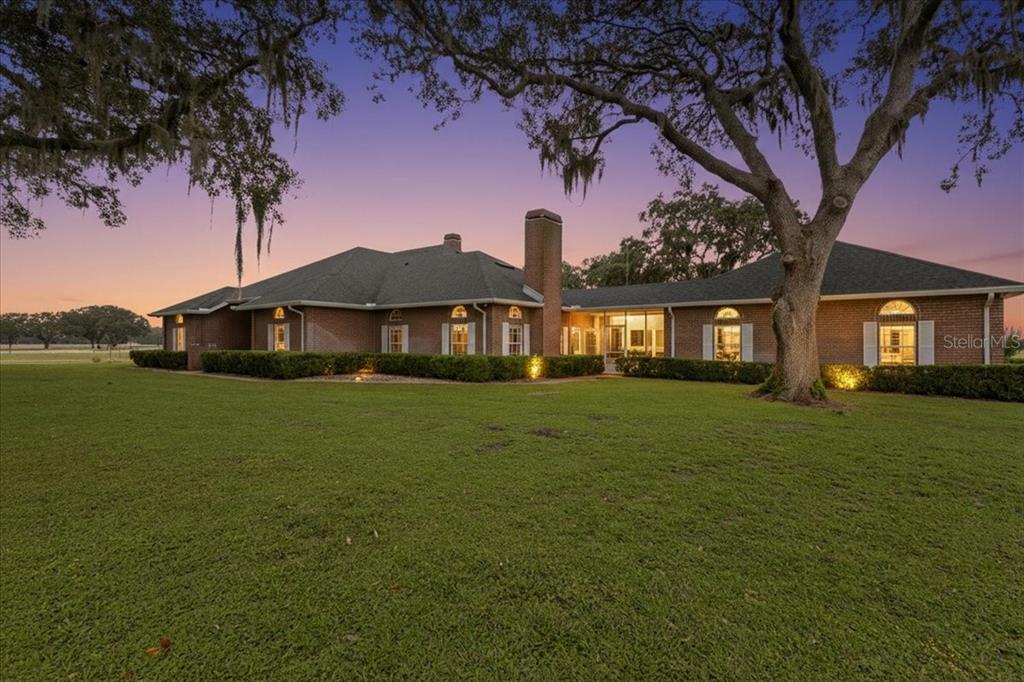 A single-story brick house with a large lawn and mature trees at twilight — 10151 NW 70TH STREET, CHIEFLAND, FL