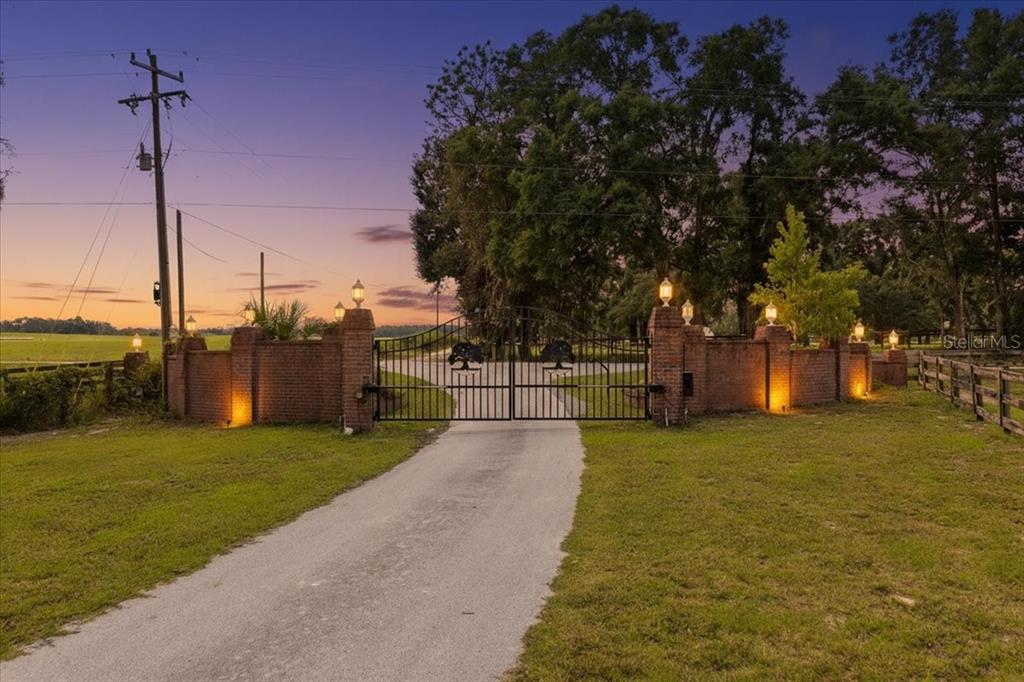 A paved driveway leads to a gated entrance with brick pillars and decorative metal fencing — 10151 NW 70TH STREET, CHIEFLAND, FL